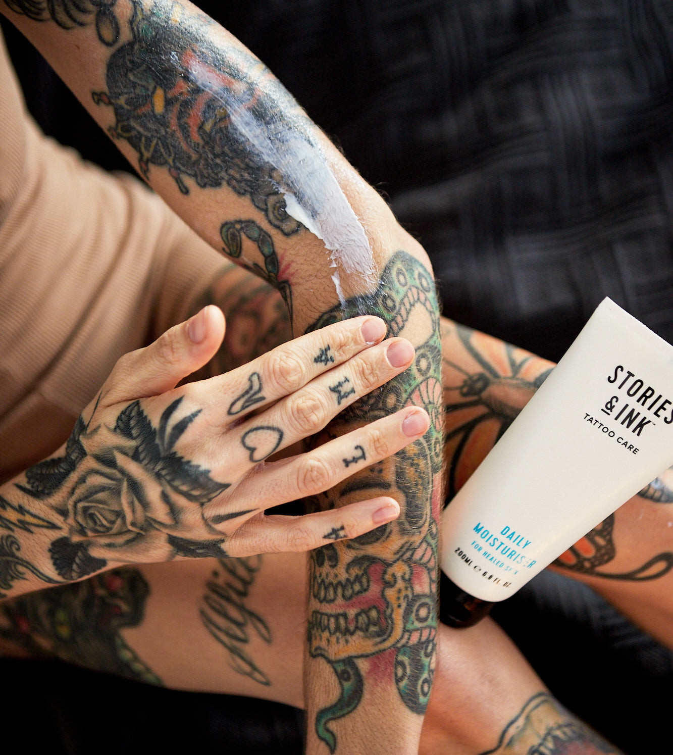 Close up of a person applying lotion to their arm, highlighting skin preparation for a tattoo.