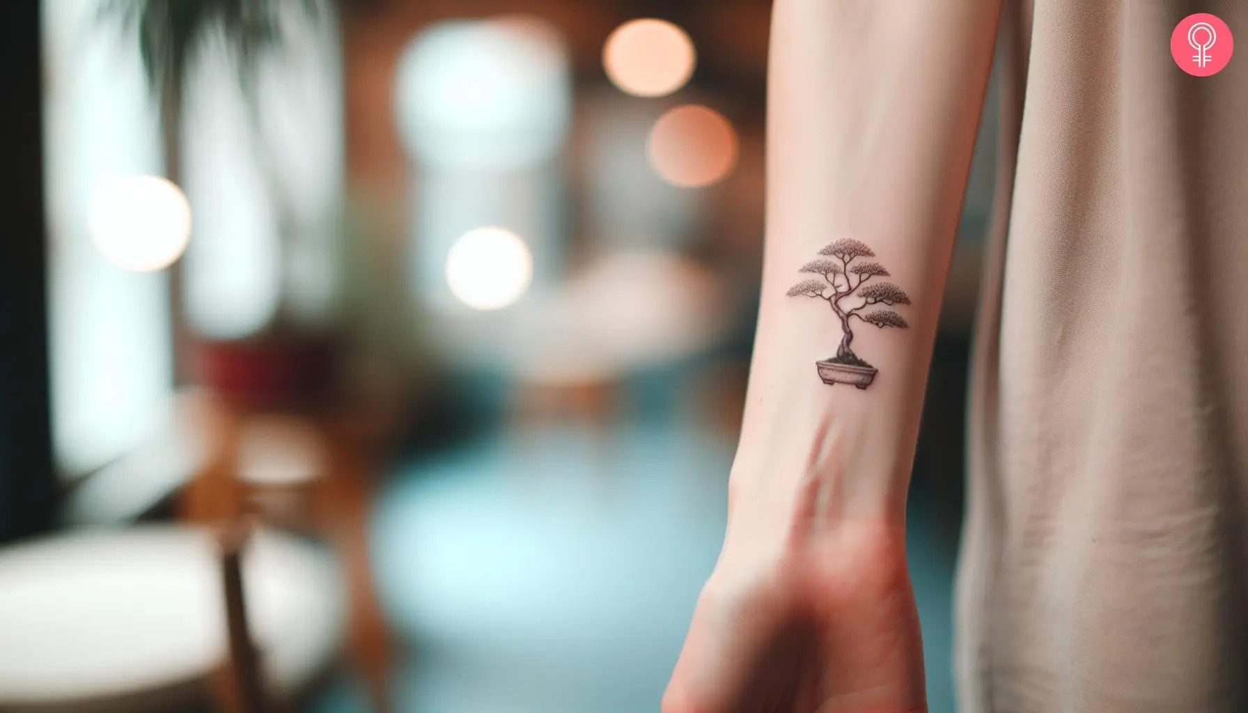 A woman's wrist is adorned with a minimalist bonsai tree tattoo, symbolizing harmony and inner peace through its clean and sophisticated design.