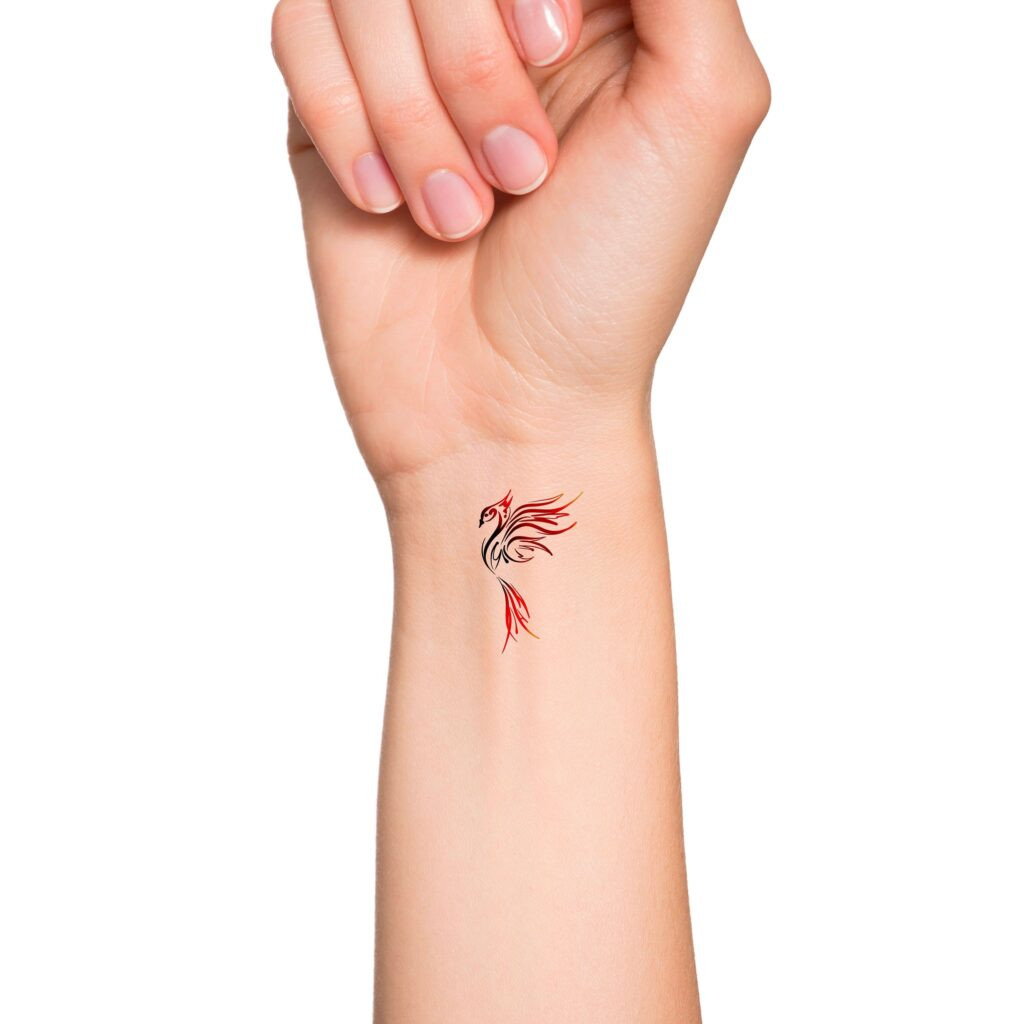 Close-up of a wrist with a colorful phoenix tattoo design, showcasing intricate red and black lines on light skin.