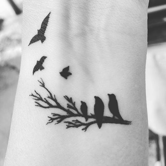 Black ink birds flying from branch miscarriage tattoo on forearm.