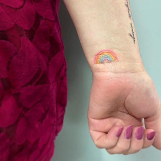 Rainbow watercolor style miscarriage tattoo on arm.