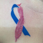 Pink and blue ribbon and feather miscarriage tattoo on forearm.