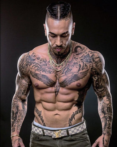 Muscular man with full sleeve tattoos featuring skulls, roses, and barbed wire in a tough style