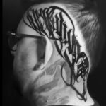 Lettering tattoo on the side of the head featuring the word "GRATITUDE" in cursive font.