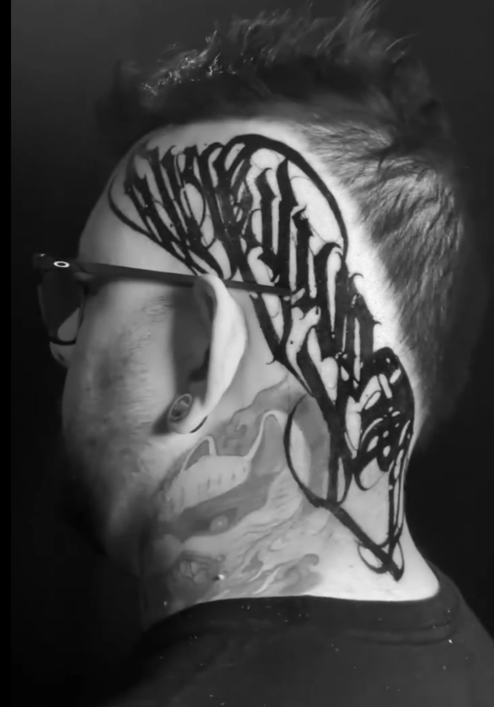 Lettering tattoo on the side of the head featuring the word "GRATITUDE" in cursive font.