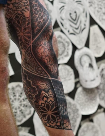 Ornamental blackwork tattoo design for men, creating a carved or textured effect with intricate patterns.