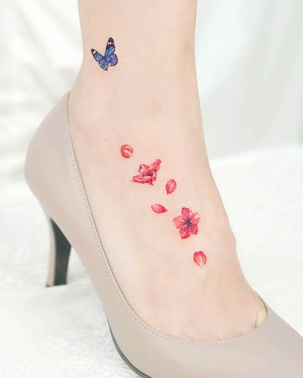 Petals and butterfly foot tattoo, featuring contrasting colors and scattered motifs for a subtle yet bold feminine design