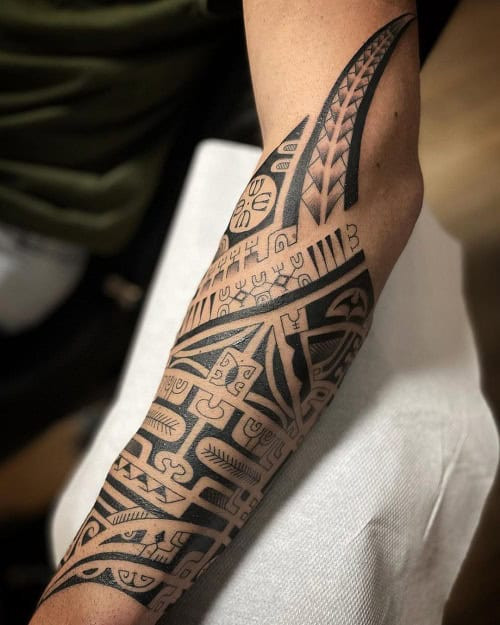 Polynesian tribal tattoo on a man's arm and shoulder, featuring complex patterns and flowing lines.