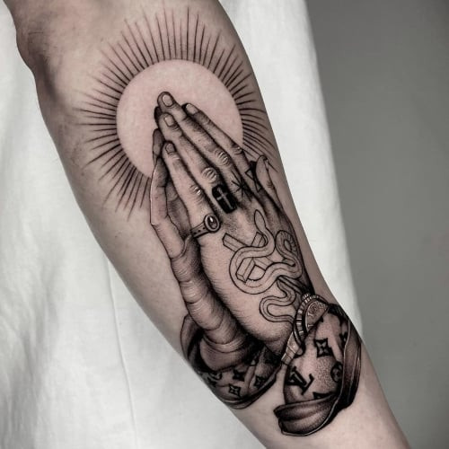 A praying hands tattoo with rosary beads on a man's arm, symbolizing devotion