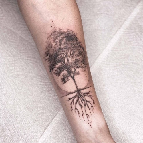 A tree roots tattoo extending upwards on a man's arm, symbolizing growth and ancestry