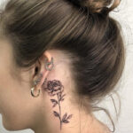 Detailed red rose tattoo on the side of a neck, showcasing vibrant petals and green leaves.