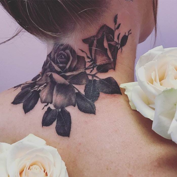 Discreet small black ink rose tattoo placed on the nape of a woman's neck, subtle and elegant.