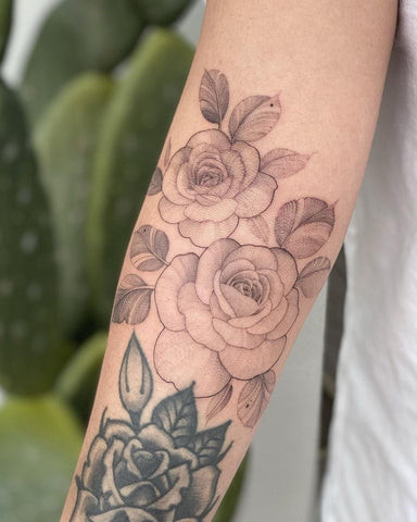 Forearm tattoo featuring three red roses with green leaves, depicted in a traditional tattoo style with bold outlines.