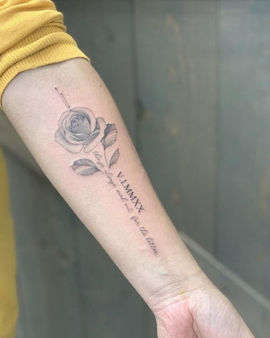 Realistic rose tattoo in full bloom on a man's forearm, rendered in black and gray with detailed thorns and leaves.