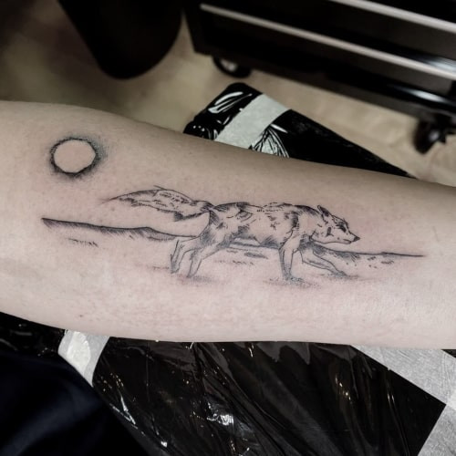 A running wolf tattoo on a man's leg, depicting a wolf in motion with flowing lines, symbolizing freedom, a wild spirit, and the journey of life.