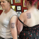 Two friends displaying their matching tarot card tattoos, one with a sun design and the other with a moon, inked by Sarah Louise to represent balance in friendship.