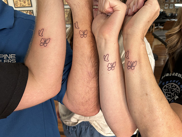 A family displaying matching butterfly tattoos on their forearms, symbolizing their shared journey with Savannah's ependymoma.