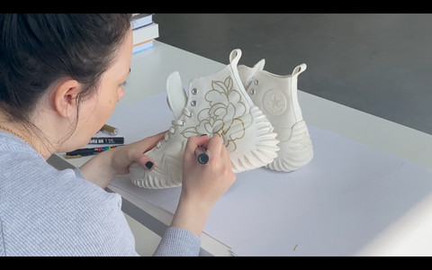 Drawing floral patterns on canvas shoes with gold paint marker, illustrating detailed artwork