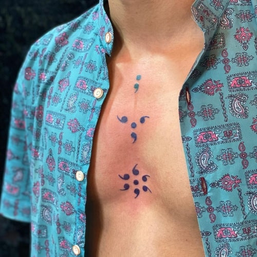 A semicolon tattoo incorporated into a design on a man's arm, subtle hope symbol