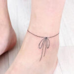 Delicate string anklet tattoo wrapping around the ankle with a ribbon, embodying minimalist and girly style