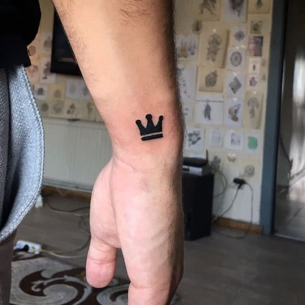 Simple crown outline tattoo on wrist, minimalist black ink design for men.