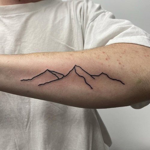 Simple mountain range tattoo on wrist, minimalist outline design for men.