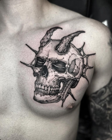 Man with a skull chest tattoo featuring a detailed skull with intricate designs