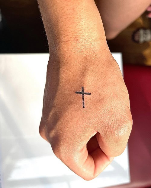 Small black ink cross tattoo on a man's hand