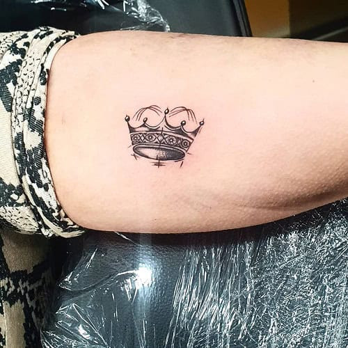 Small crown tattoo with delicate linework on a man's finger