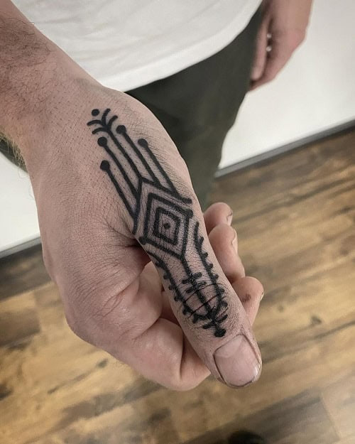 Small tribal tattoo on a man's wrist, featuring a minimalist tribal design in black ink.