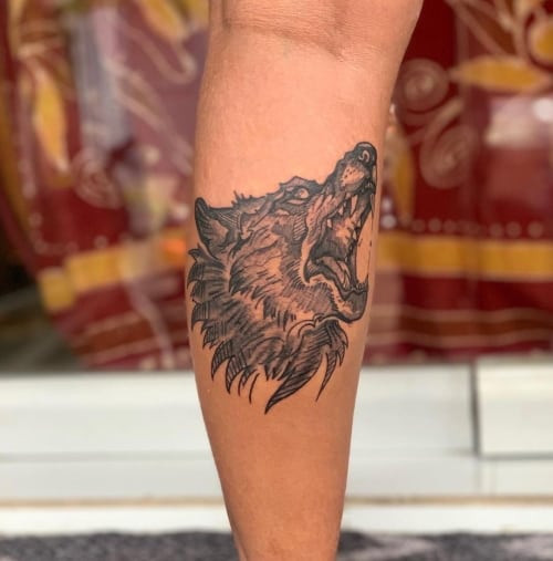 A small and discreet wolf tattoo on a man's wrist, rendered in black and grey with fine lines, representing subtle strength and personal meaning in a minimalist style.