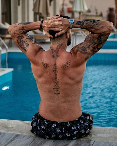 A man displaying a small, subtle back tattoo on his upper back