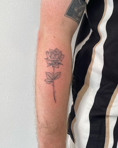 Small, minimalist rose tattoo on a forearm, using fine lines and minimal shading for a subtle and delicate design.