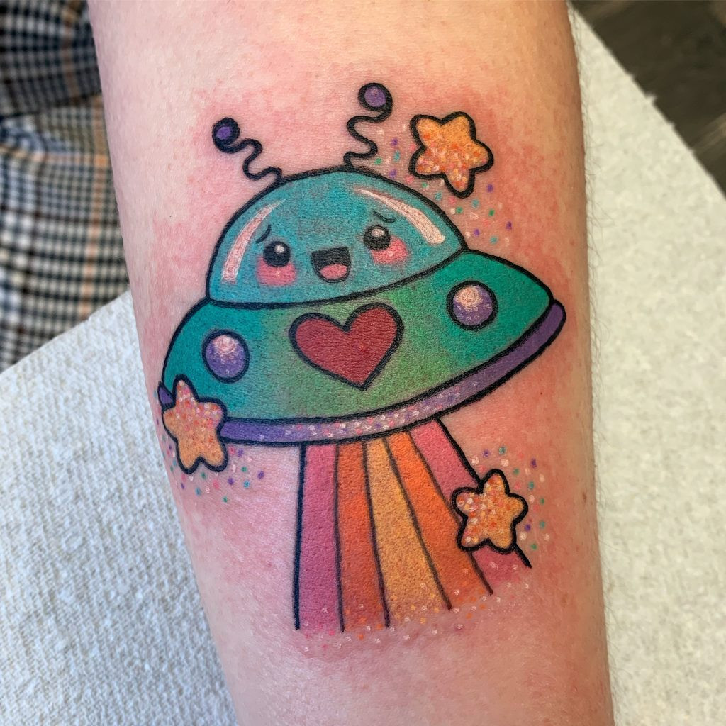 A cute spaceship tattoo with pastel colors, stars, and a whimsical, cartoon-like design.