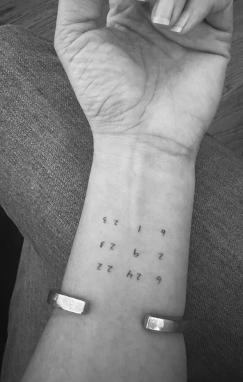 A strength tattoo showing surgery dates in a vertical line on an arm for alt text &quot;Strength tattoo listing surgery dates as milestones of survival and empowerment&quot;.