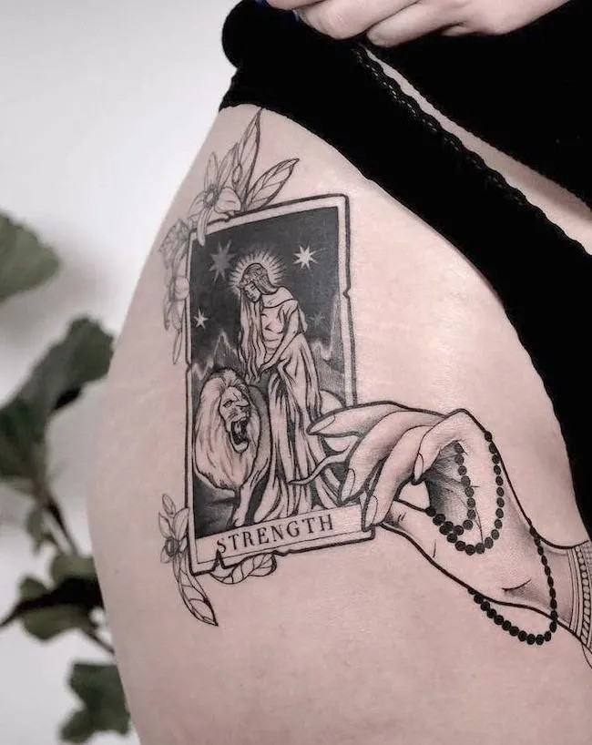 alt text:  Detailed Strength tarot card tattoo on forearm, depicting a woman gently holding a lion's mouth, representing inner strength and control