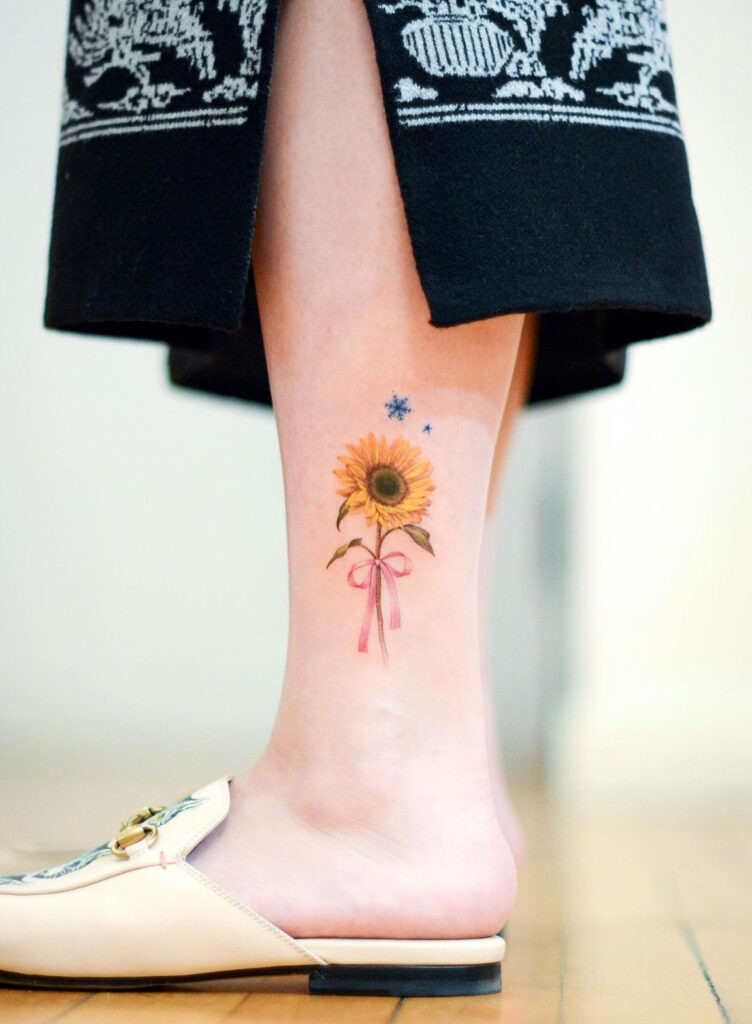 Realistic sunflower, bow, and snowflake leg tattoo