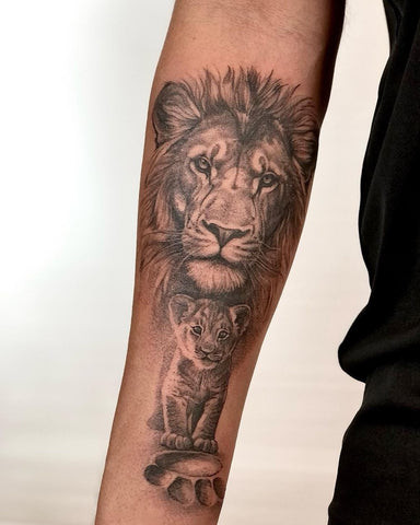 Majestic lion head tattoo on a man's outer forearm, featuring detailed mane, eyes, and shading in black and grey.