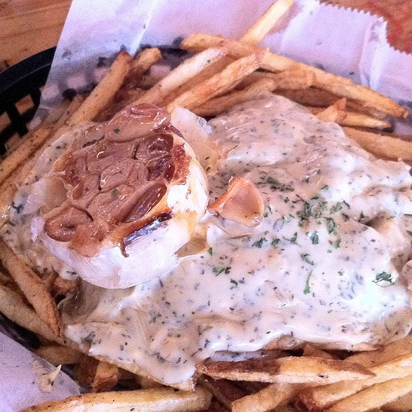 Close-up shot of golden brown duck fat fries topped with creamy blue cheese crumbles and a soft roasted garlic bulb