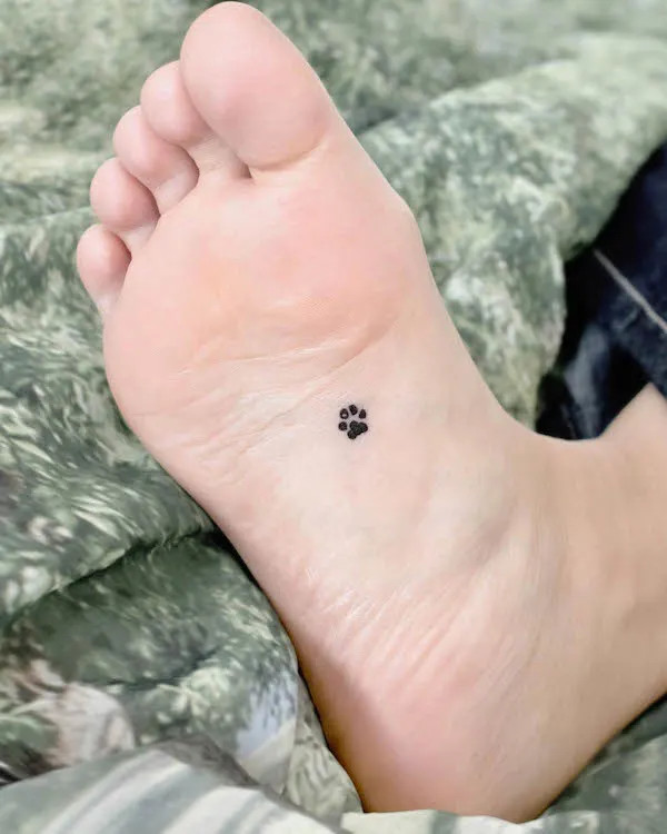 Tiny paw under the foot tattoo, an even more subtle pet tribute, showcasing a loving nature