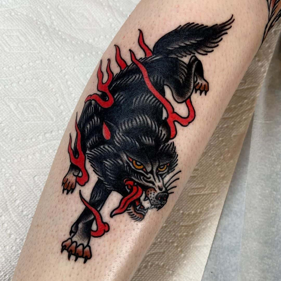 A vibrant traditional wolf tattoo on a man's arm, showcasing bold black lines, bright colors, and classic American tattoo style, symbolizing timeless strength and courage.