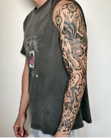 Traditional tattoo sleeve featuring bold lines and classic motifs like anchors, roses, and eagles, in vibrant primary colors.