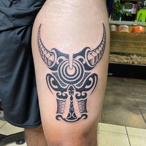 Tribal bull tattoo on a man's shoulder, depicting a bull's head with sharp horns and tribal patterns.