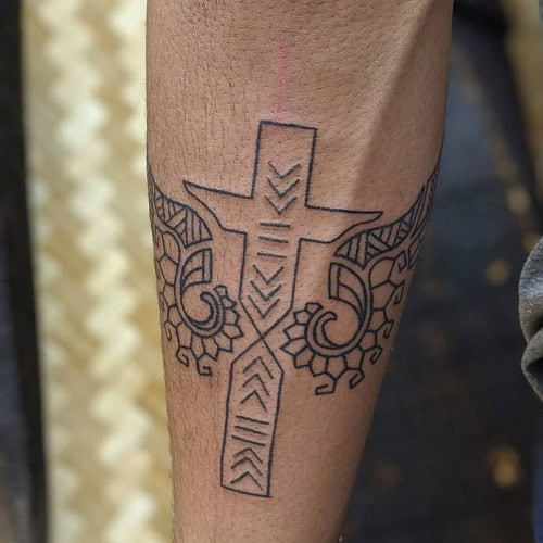 Tribal cross tattoo on a man's forearm, displaying a cross with tribal patterns and linework.