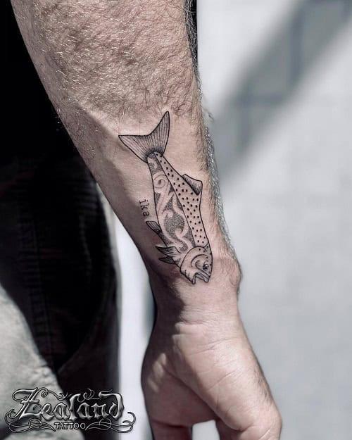 Tribal fish tattoo on a man's arm, depicting a fish with tribal patterns and flowing lines.