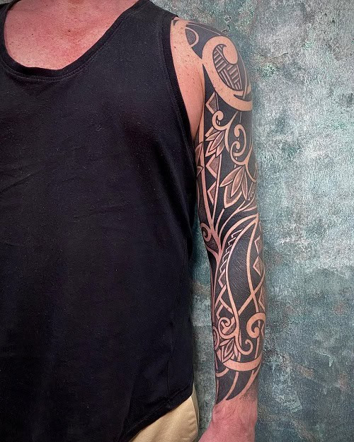 Tribal flower tattoo on a man's arm, depicting a stylized flower with tribal linework and shading.