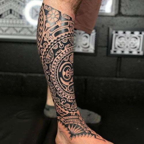 Tribal leg tattoo on a man's leg, showcasing a large tribal design covering a significant portion of the leg.