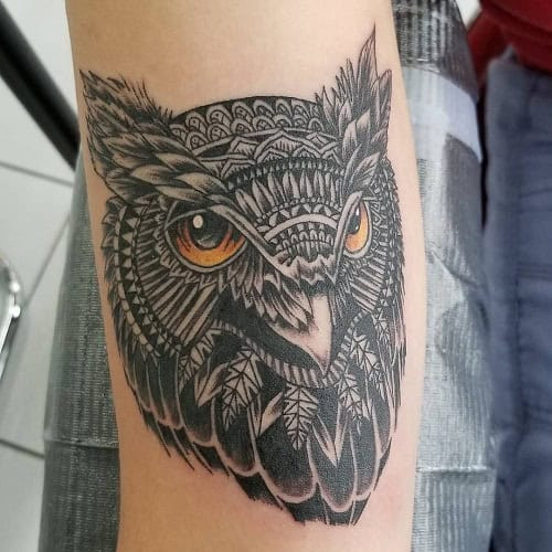 Tribal owl tattoo on a man's arm, depicting an owl with large eyes and tribal patterns incorporated into its feathers.