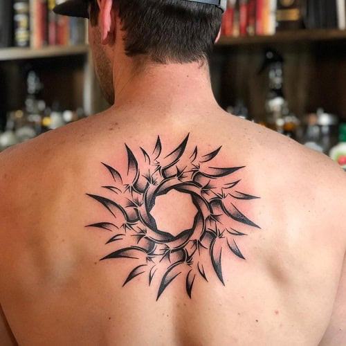 Tribal sun tattoo on a man's arm, featuring radiating lines and geometric shapes in black ink.