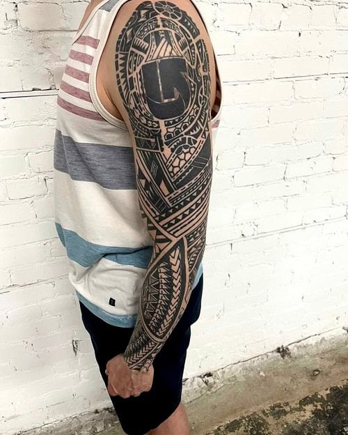 Tribal tattoo sleeve on a man's arm, showcasing a full sleeve design with intricate tribal patterns.